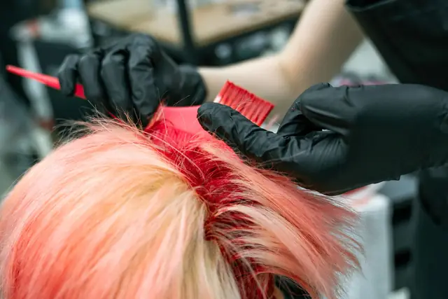 Gloved hands brushing red colour into blonde hair at the roots