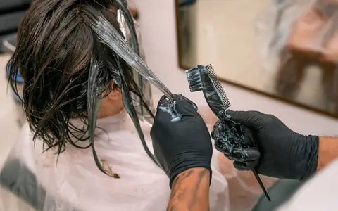 Gloved hands brushing colour through wet hair