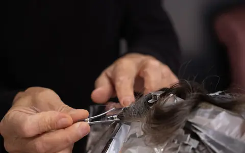 Hands sectioning dark hair over foil for highlights
