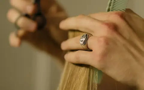 Hands trimming a lock of blonde hair with scissors and a comb