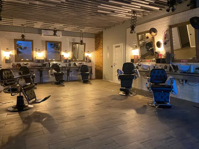 An empty salon at dusk: black styling chairs facing mirrors under warm bulb lights