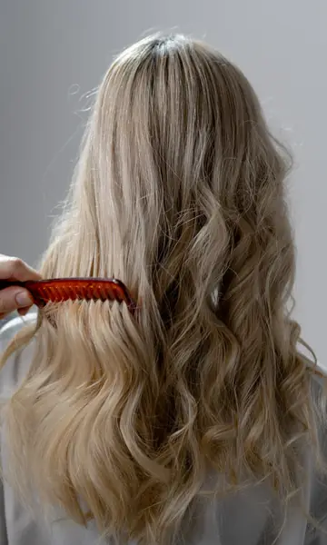 Long wavy blonde hair being combed, seen from behind